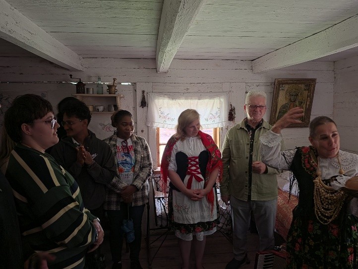 A group of people in traditional attire gathers in a rustic room, engaged in conversation and cultural exchange.